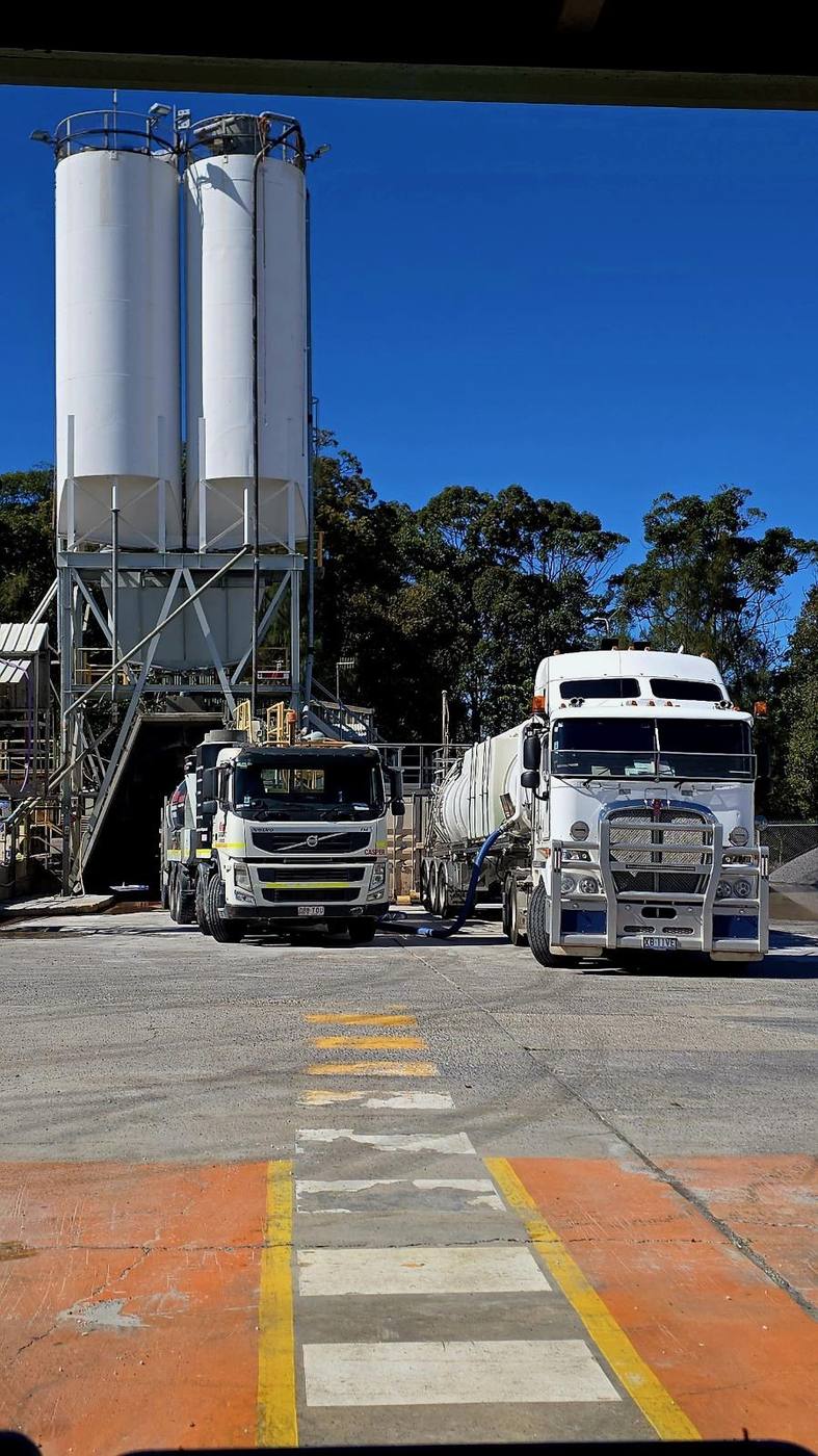 KVAC trucks Casper and a Kenworth unit parked beneath silos at an industrial batching plant