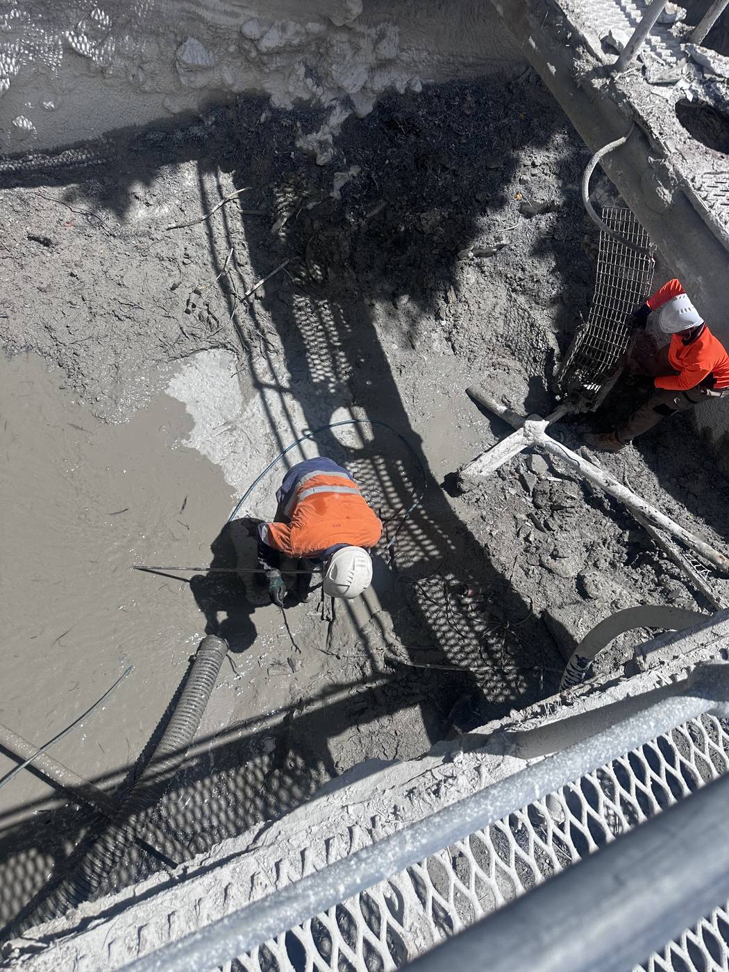 Overhead view of two KVAC operators working inside a large sludge pit