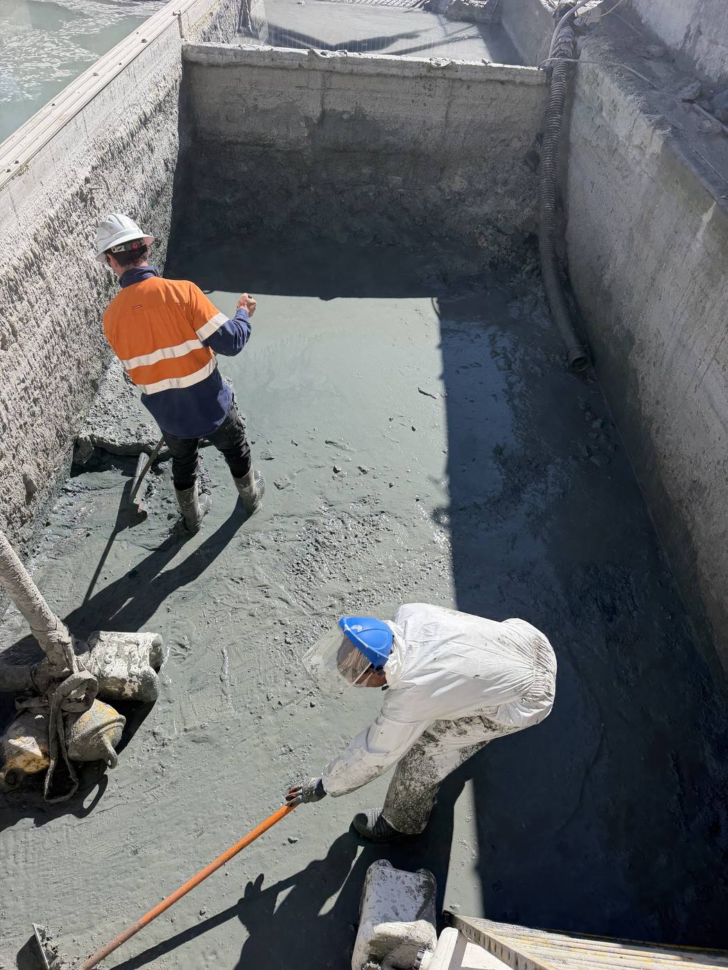 Two KVAC operators cleaning a concrete tank, one in hi-vis and one in protective coveralls
